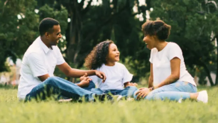 Family of 3 smiling while playing outside in the grass