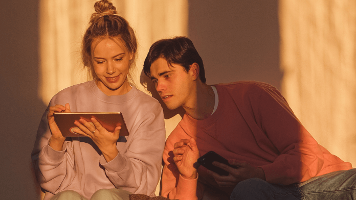 Couple looking at tablet together while sitting against a wall