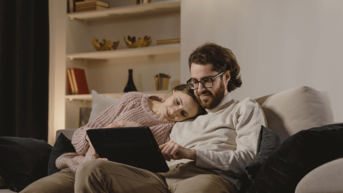 woman laying her head on man's shoulder as they look at laptop screen together