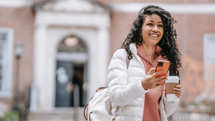 Young woman smiling while using mobile smart phone in front of building outside