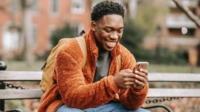 Man messaging on a phone while smiling and wearing a backpack.