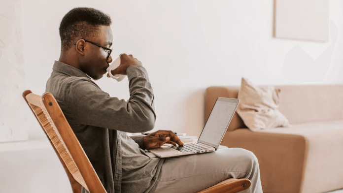 A man drinks coffee while working on a laptop.