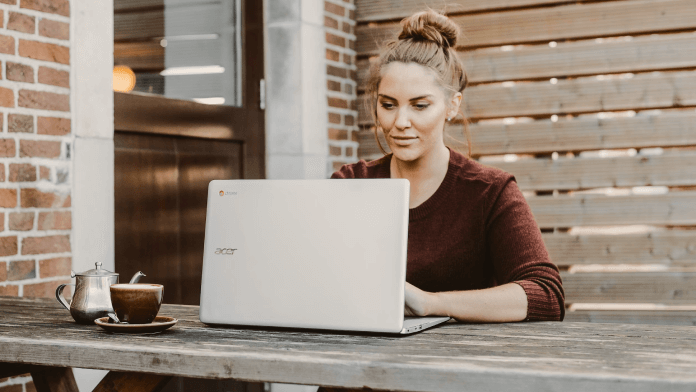 Women working on laptop, while wearing red top, on the wooden table. 