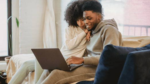 Young couple wearing lounge wear while smiling and looking at laptop together