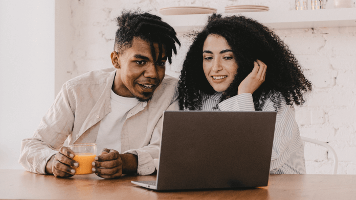 A guy holding a glass of juice is watching laptop along with a girl.